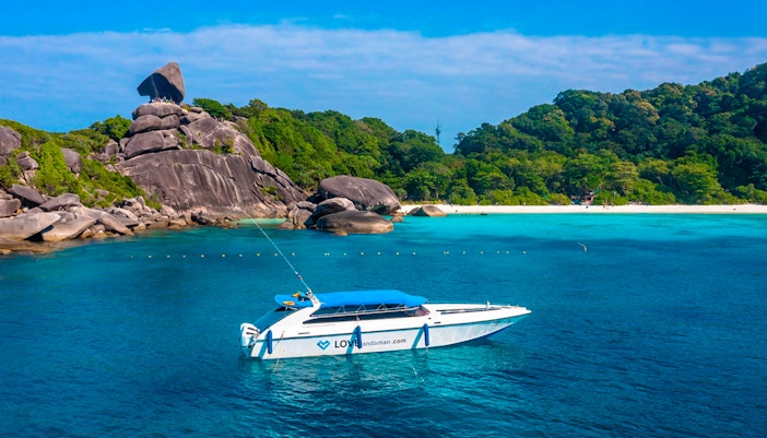 Speedboat near Similan Islands with rocky shoreline and lush greenery.