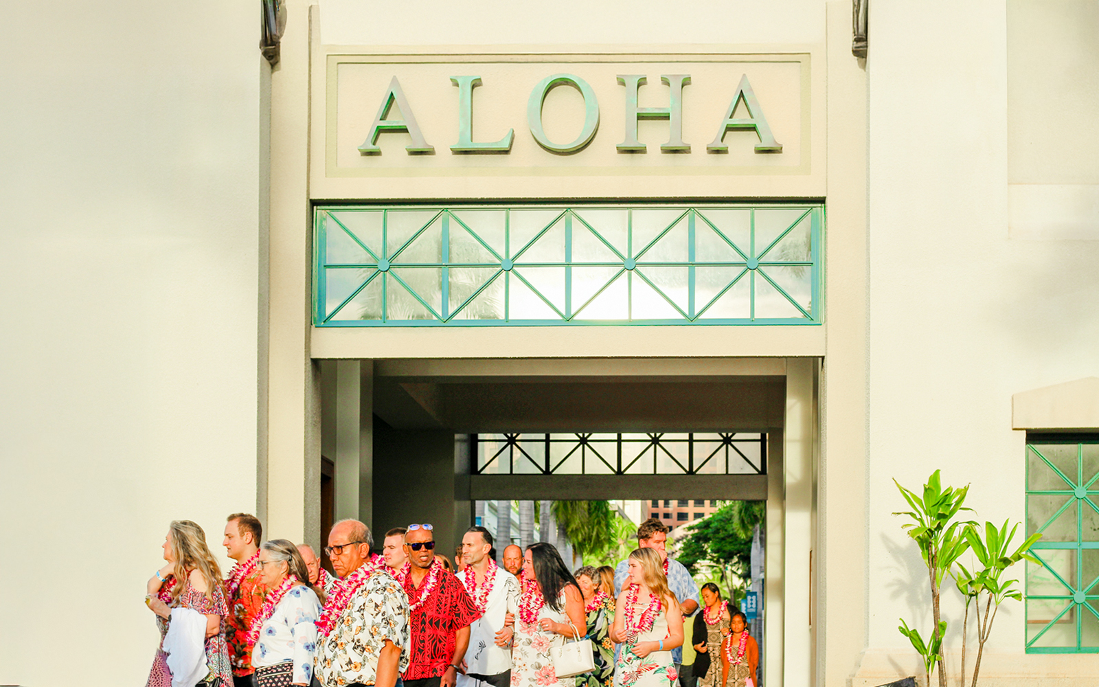 Guests arriving at Moana Luau, Hawaii, wearing leis under an "Aloha" sign.