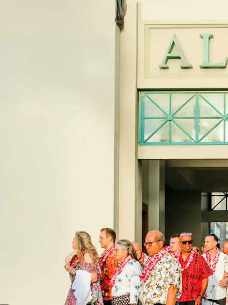 Guests arriving at Moana Luau, Hawaii, wearing leis under an "Aloha" sign.