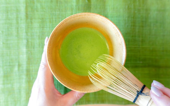 Preparing matcha green tea with a bamboo whisk in a ceramic bowl.