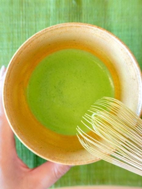 Preparing matcha green tea with a bamboo whisk in a ceramic bowl.