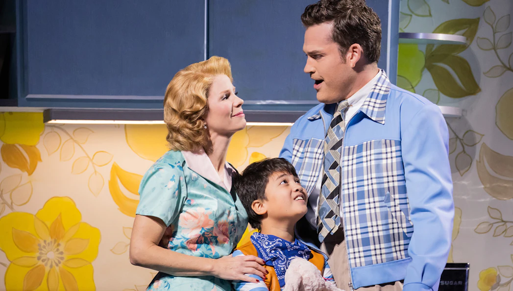 Family scene from "The Hours" musical with a woman, man, and child in a kitchen setting.