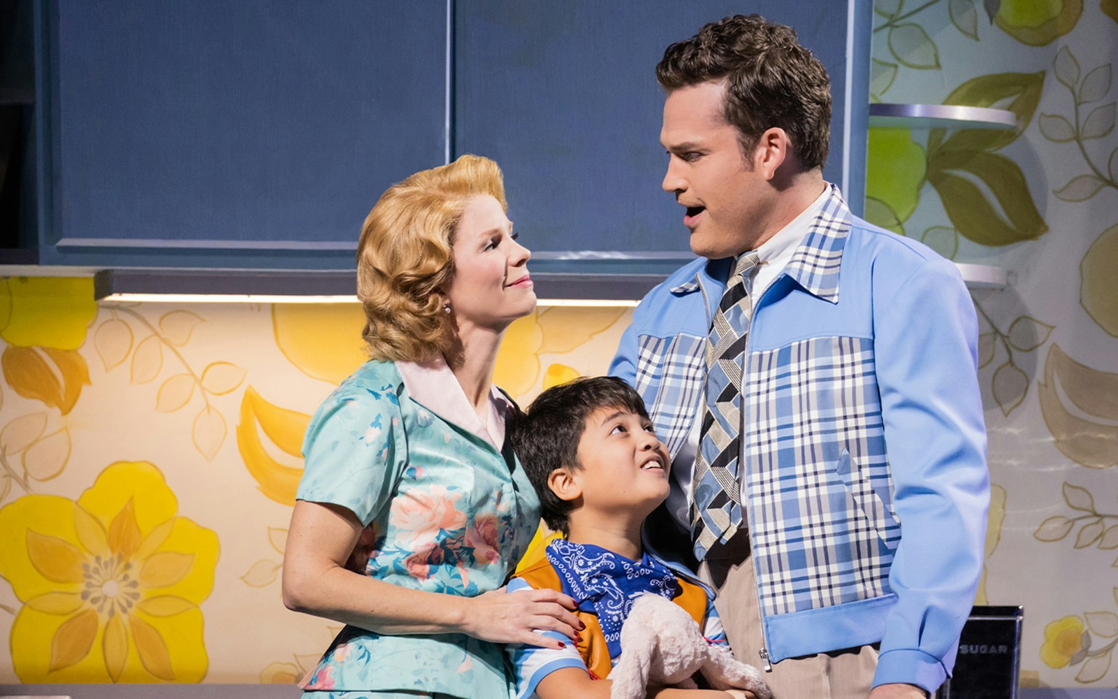 Family scene from "The Hours" musical with a woman, man, and child in a kitchen setting.