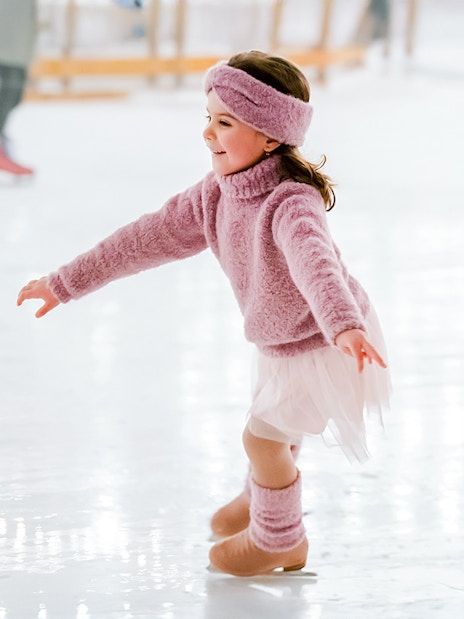 Little girl in pink sweater ice skating indoors.