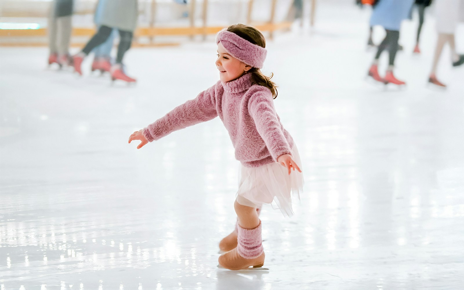 Little girl in pink sweater ice skating indoors.