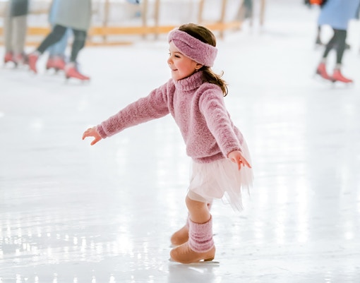 Little girl in pink sweater ice skating indoors.