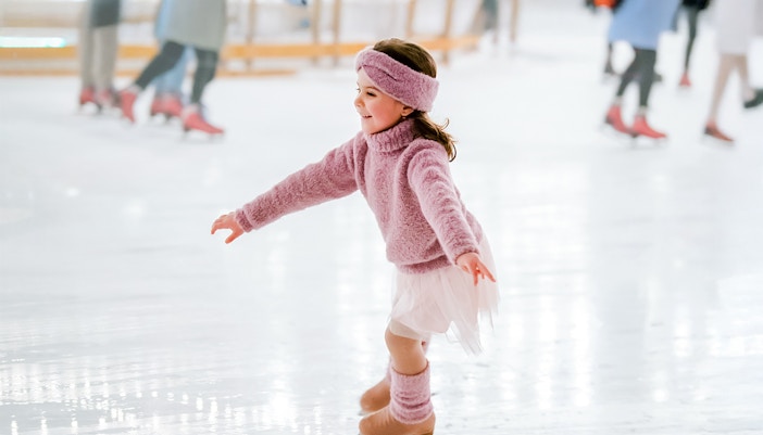 Little girl in pink sweater ice skating indoors.