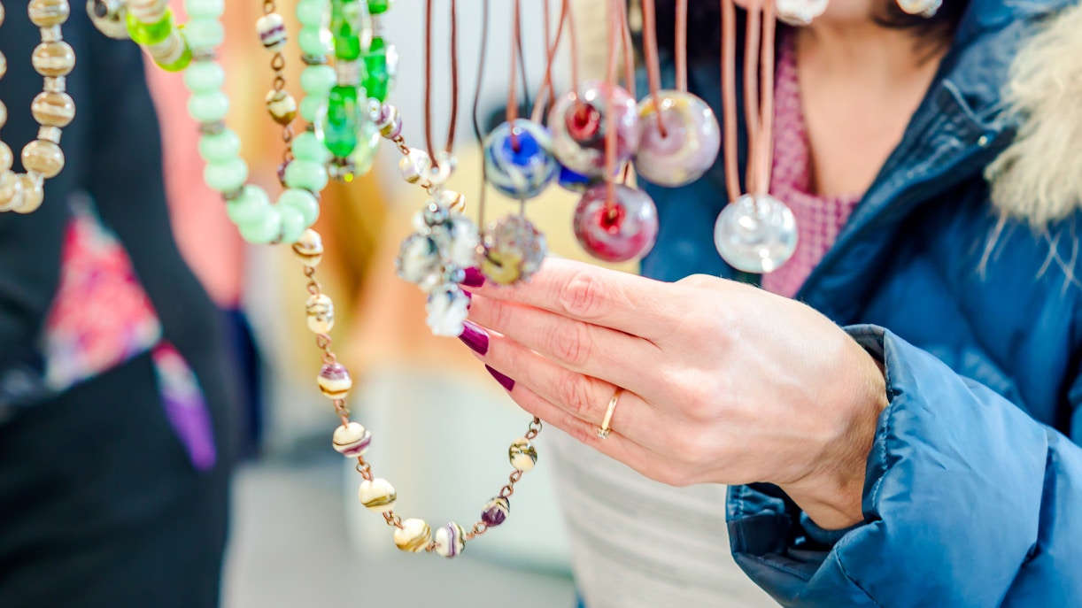 Brunette woman in blue coat selecting necklaces at a flea market.