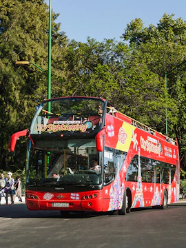 Red double-decker bus for city sightseeing in Madrid, surrounded by trees.