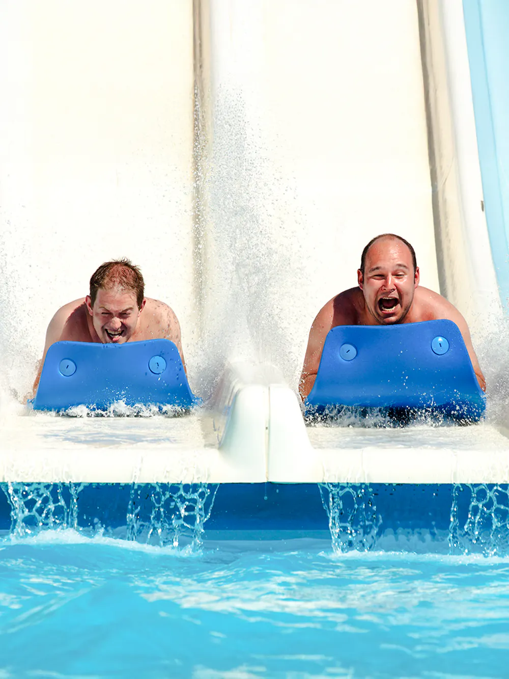 Two people sliding down a water slide on mats at a water park.