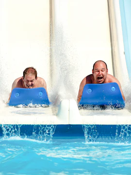 Two people sliding down a water slide on mats at a water park.