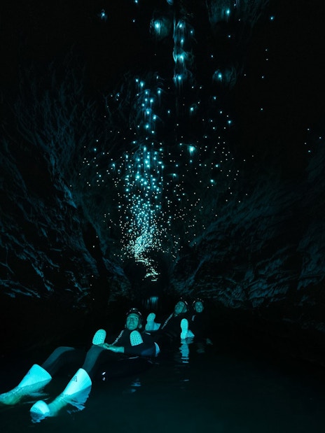 Visitors floating in Okohua Glowworm Cave, illuminated by glowworms above.