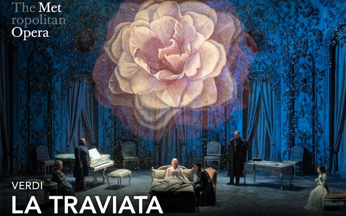 Opera scene from La Traviata at the Metropolitan Opera with a large flower backdrop.