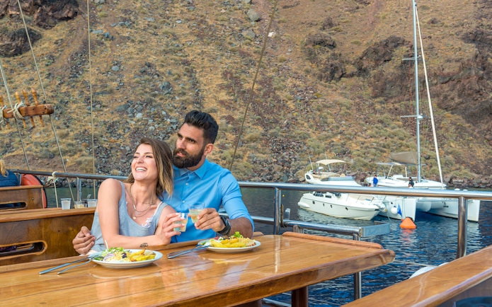 Couple dining on a boat near volcanic islands with yachts in the background.