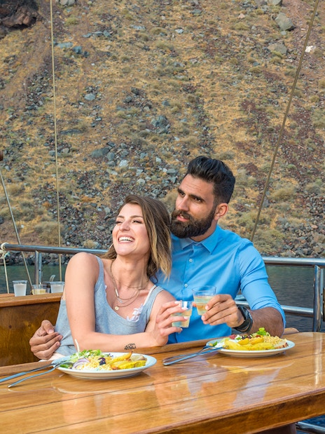 Couple dining on a boat near volcanic islands with yachts in the background.