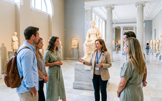 Tour group with guide at National Archaeological Museum, Athens, near ancient statue.
