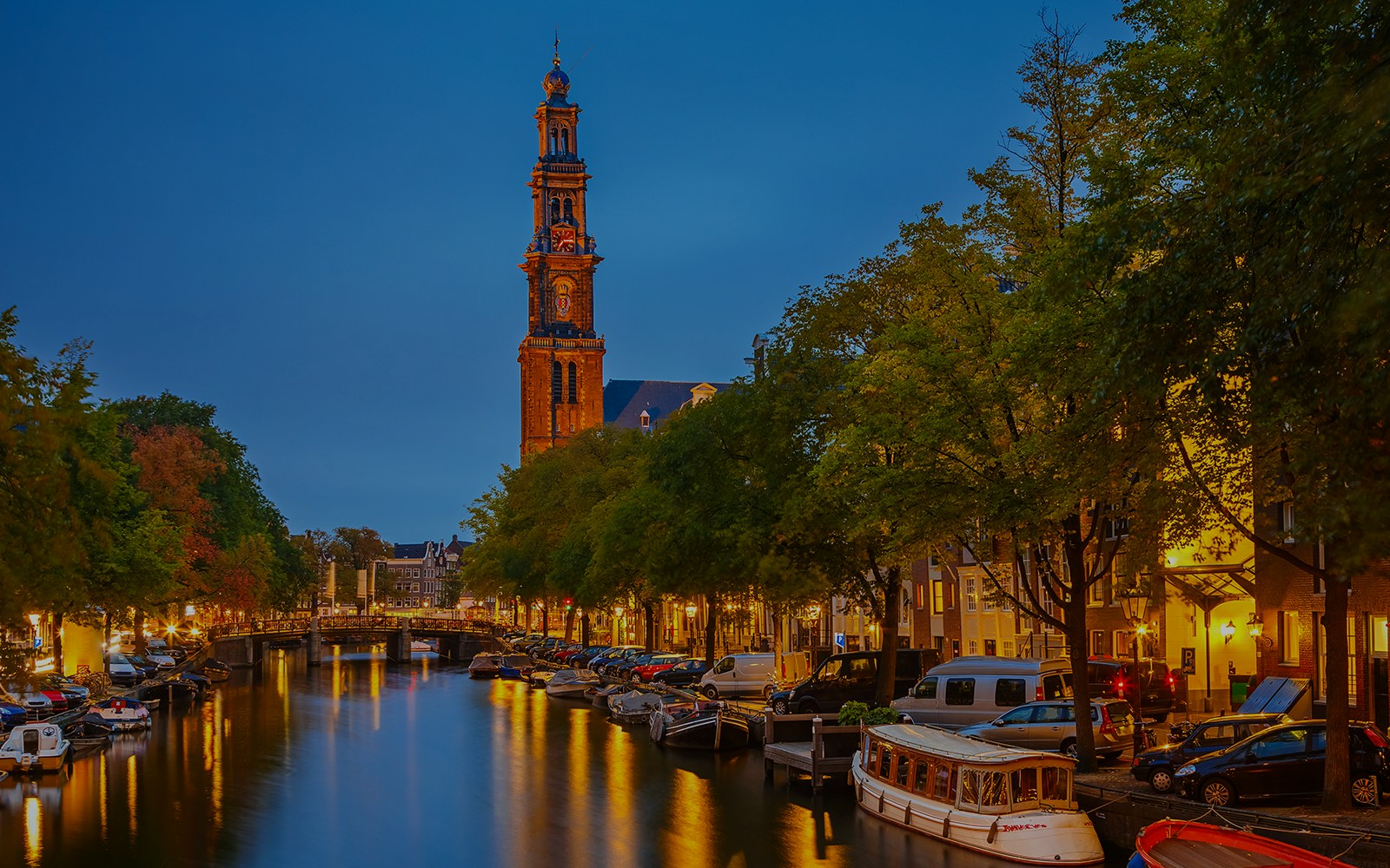 Westerkerk tower illuminated at night along Amsterdam canal.