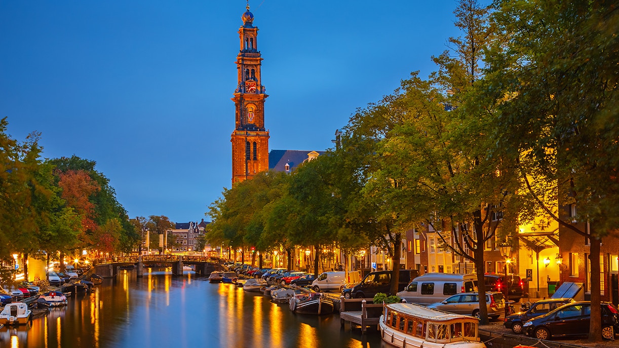 Westerkerk tower illuminated at night along Amsterdam canal.