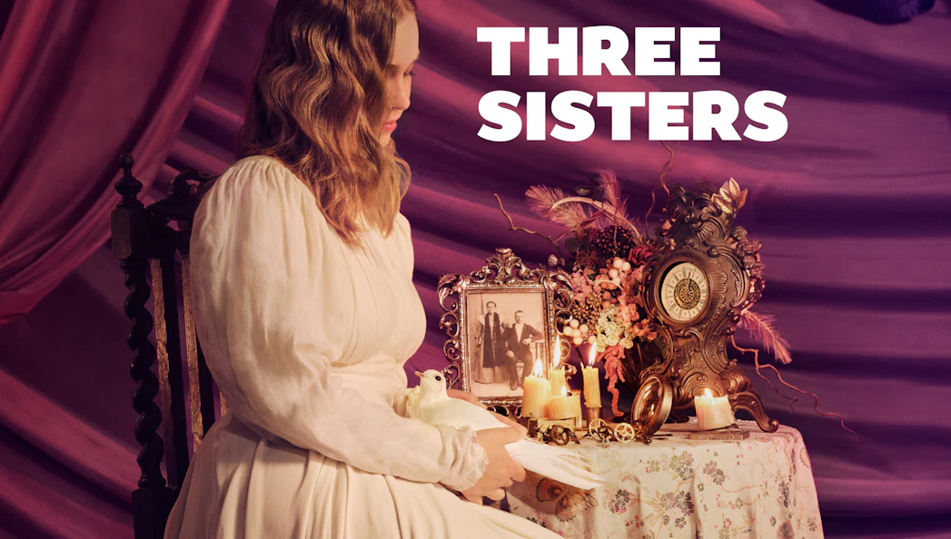 Woman in vintage dress holding a dove beside a table with candles, clock, and old photo labeled "Three Sisters.