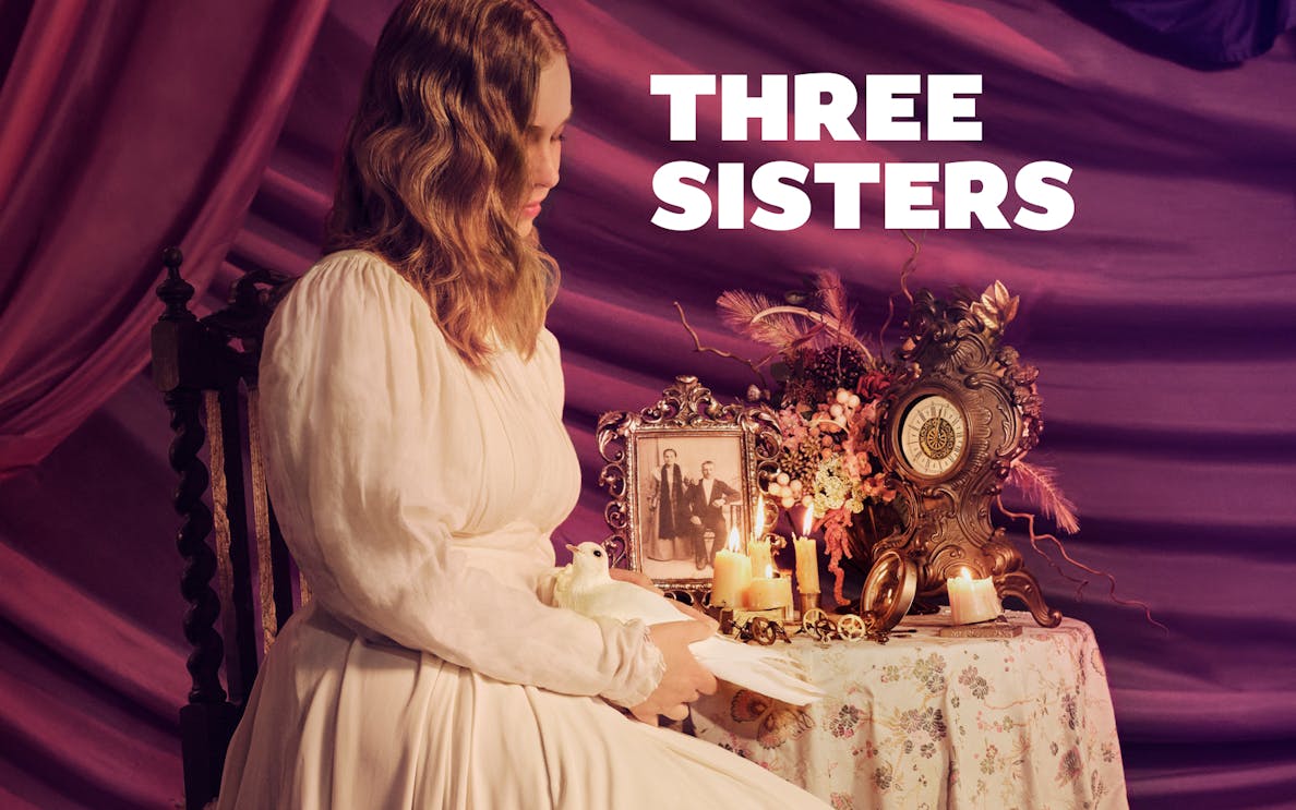 Woman in vintage dress holding a dove beside a table with candles, clock, and old photo labeled "Three Sisters.