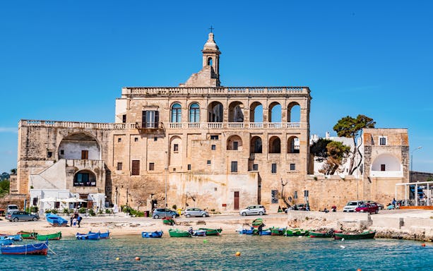 Polignano a Mare waterfront with historic building and colorful boats.