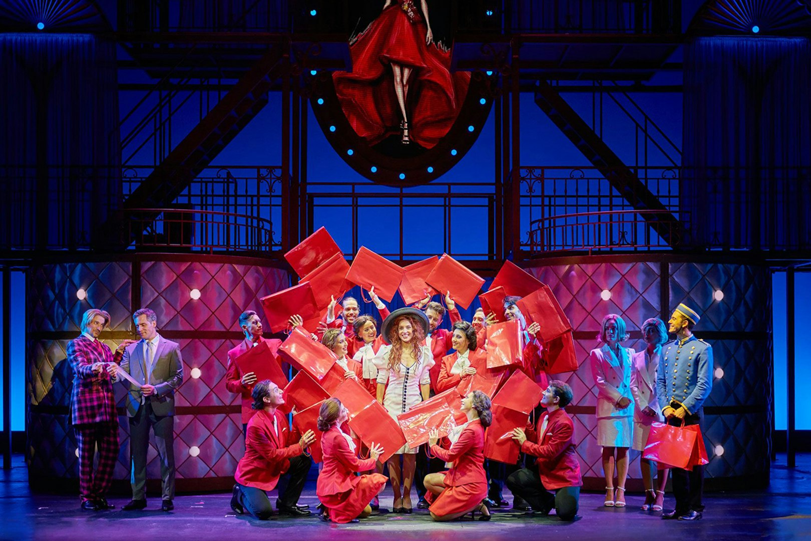 Cast performing a scene from "Pretty Woman - El musical" with red shopping bags on stage.