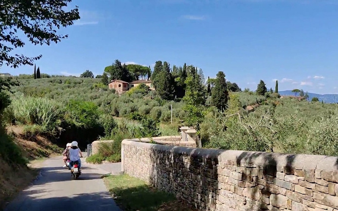 Vespa riders on a scenic road through Tuscany's countryside near Florence.