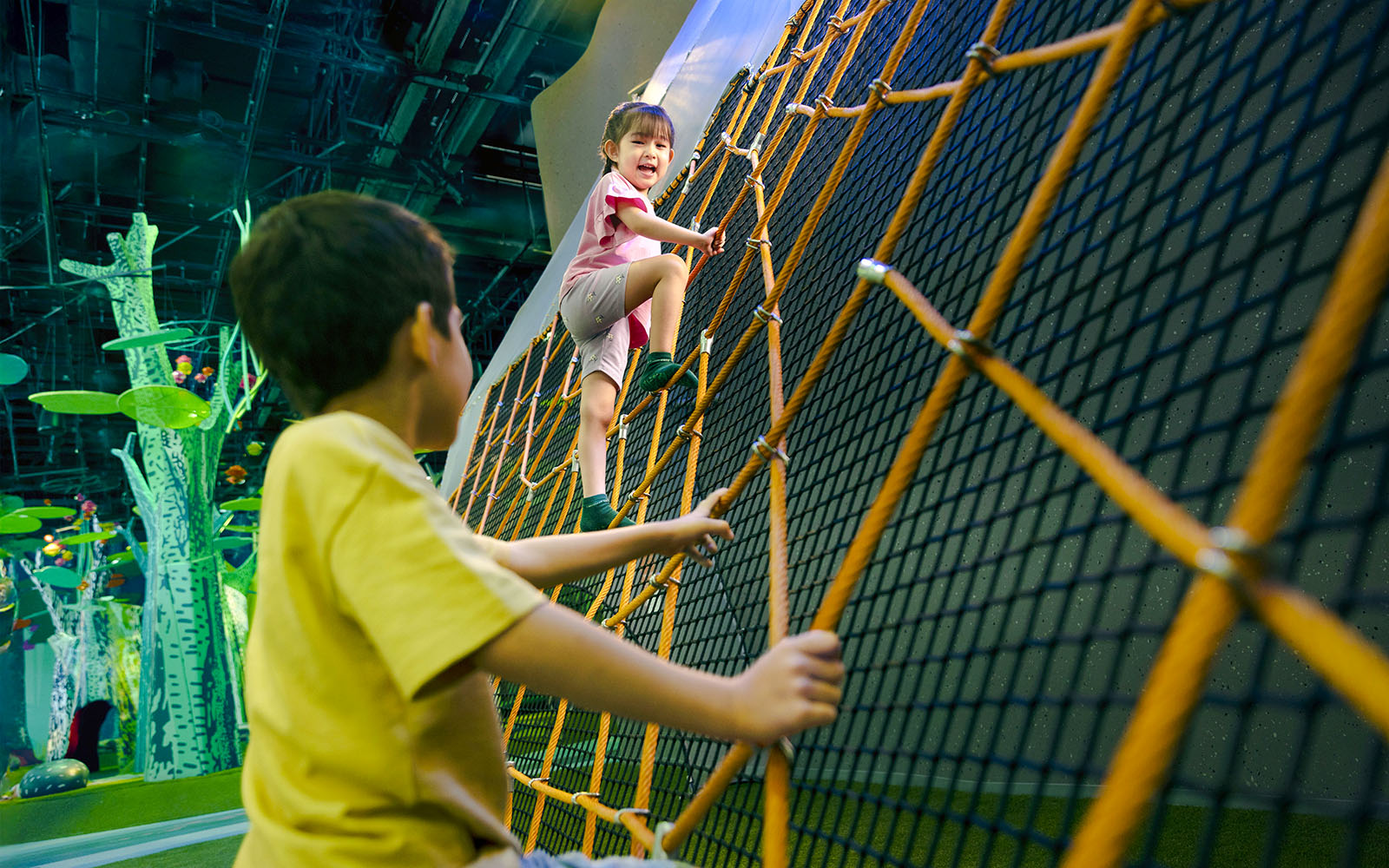 Children climbing a large net structure at Forestland Giant Spider Web attraction.