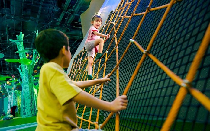 Children climbing a large net structure at Forestland Giant Spider Web attraction.