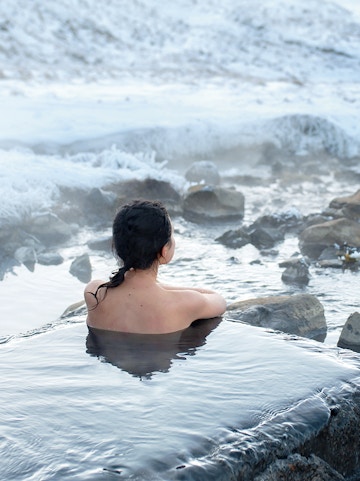 Person relaxing in Blue Lagoon geothermal spa, Iceland, surrounded by snowy landscape.