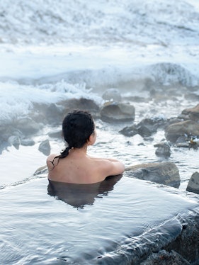 Person relaxing in Blue Lagoon geothermal spa, Iceland, surrounded by snowy landscape.