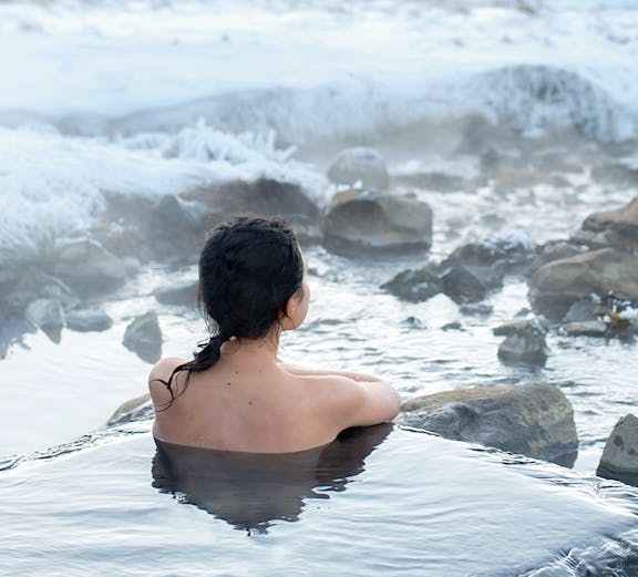 Person relaxing in Blue Lagoon geothermal spa, Iceland, surrounded by snowy landscape.