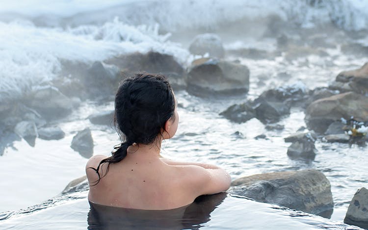 Person relaxing in Blue Lagoon geothermal spa, Iceland, surrounded by snowy landscape.