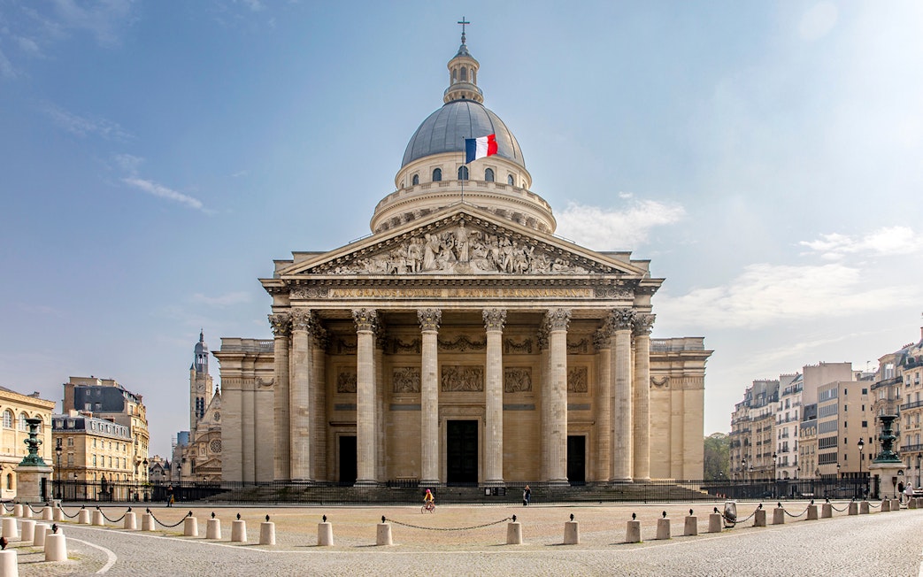 Facade of the Pantheon in Paris with French flag atop dome.