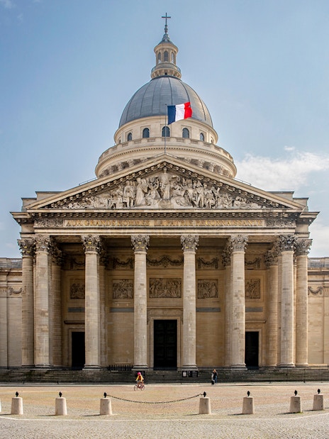 Facade of the Pantheon in Paris with French flag atop dome.