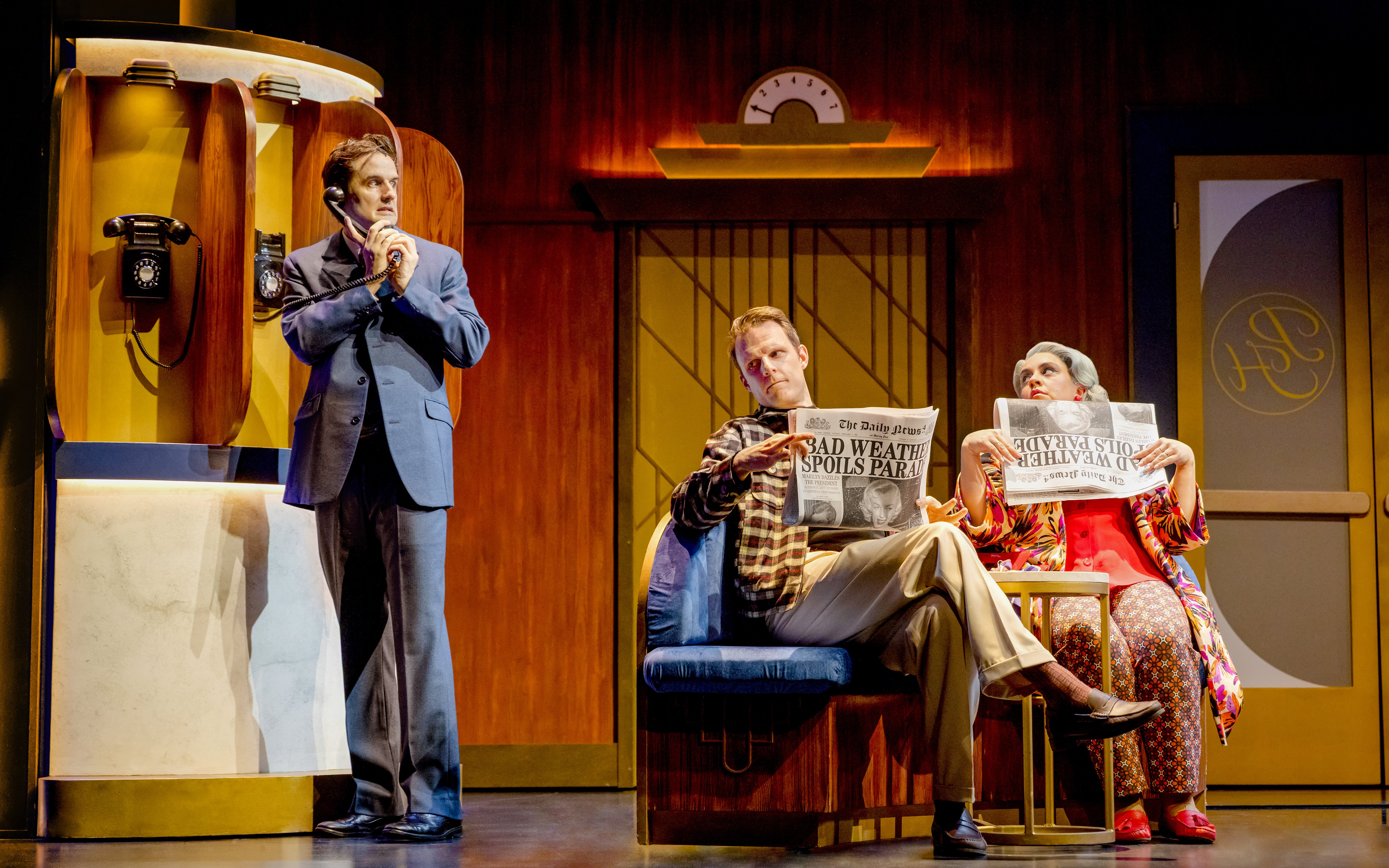 Actors in a comedic spy play scene, one on the phone, two reading newspapers on stage.
