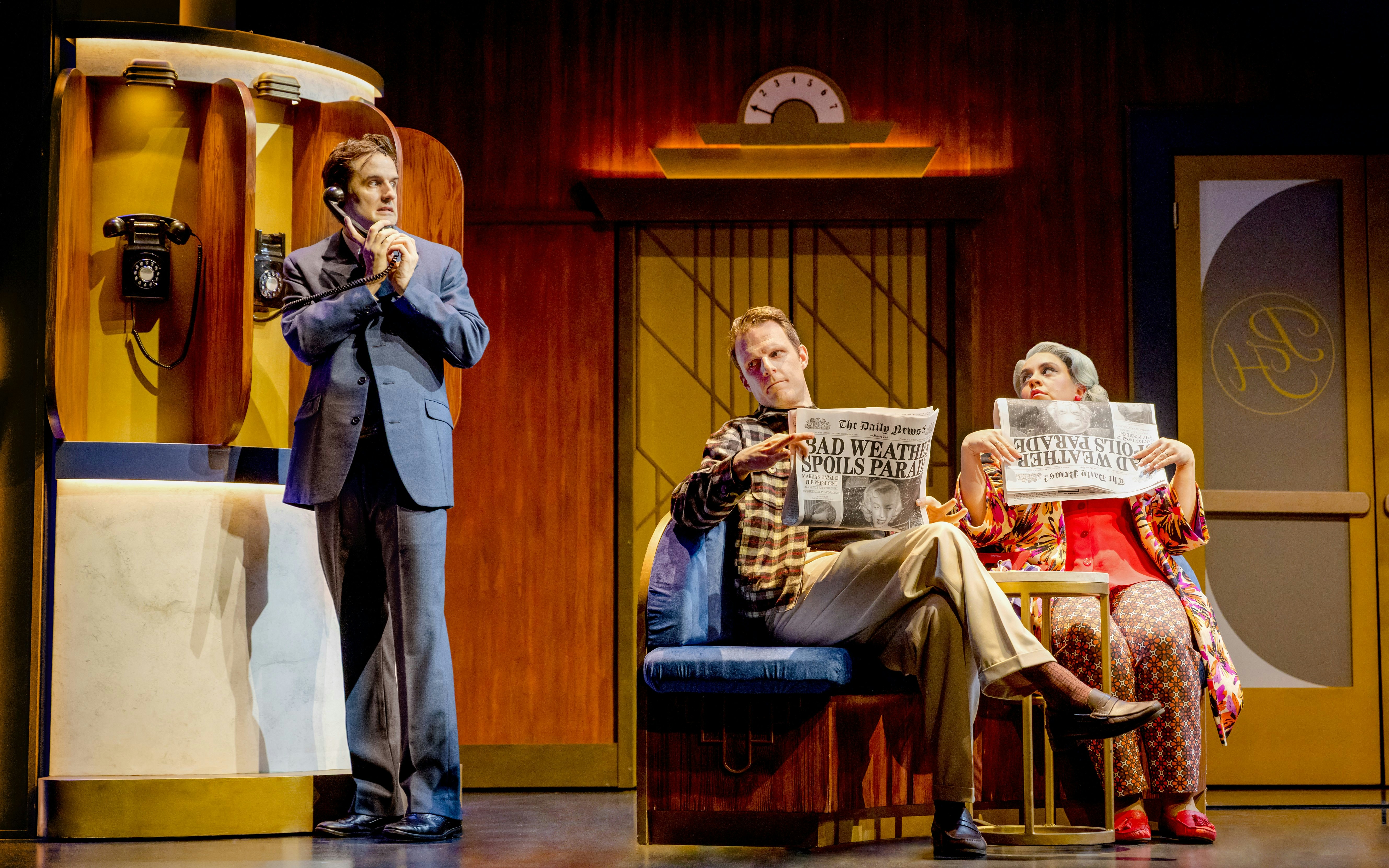 Actors in a comedic spy play scene, one on the phone, two reading newspapers on stage.