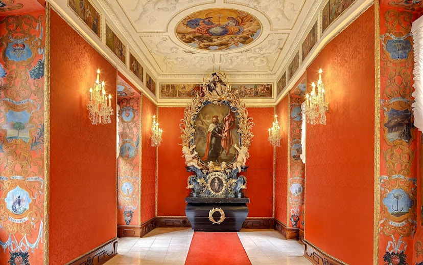 Ornate hallway with red walls and chandeliers inside Lobkowicz Palace Museum, Prague Castle.