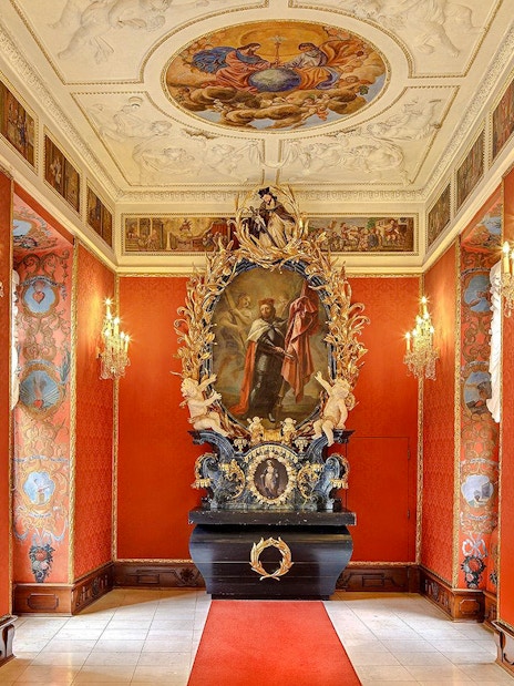 Ornate hallway with red walls and chandeliers inside Lobkowicz Palace Museum, Prague Castle.