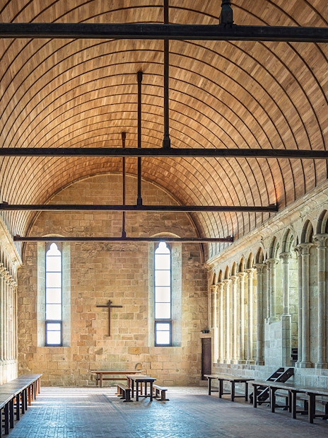 Interior of Mont St. Michel abbey with arched stone columns and wooden ceiling.