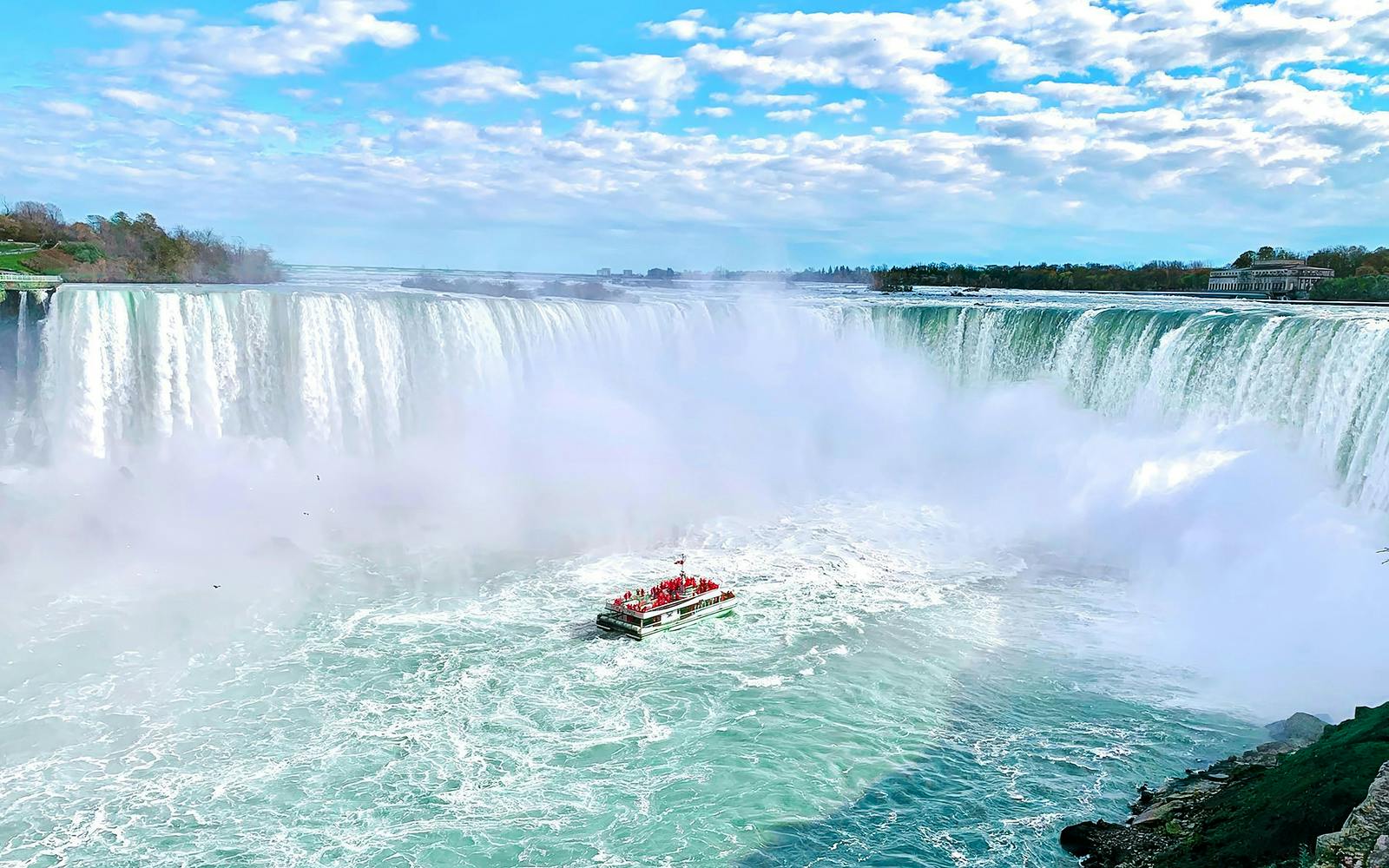 Boat approaching Niagara Falls on a tour with mist rising from the waterfall.