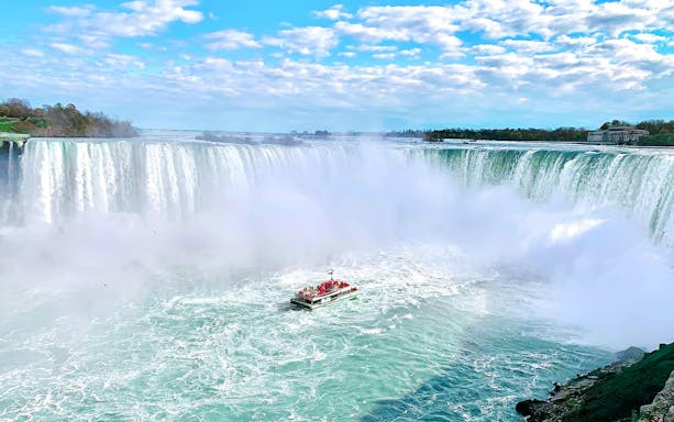Boat approaching Niagara Falls on a tour with mist rising from the waterfall.