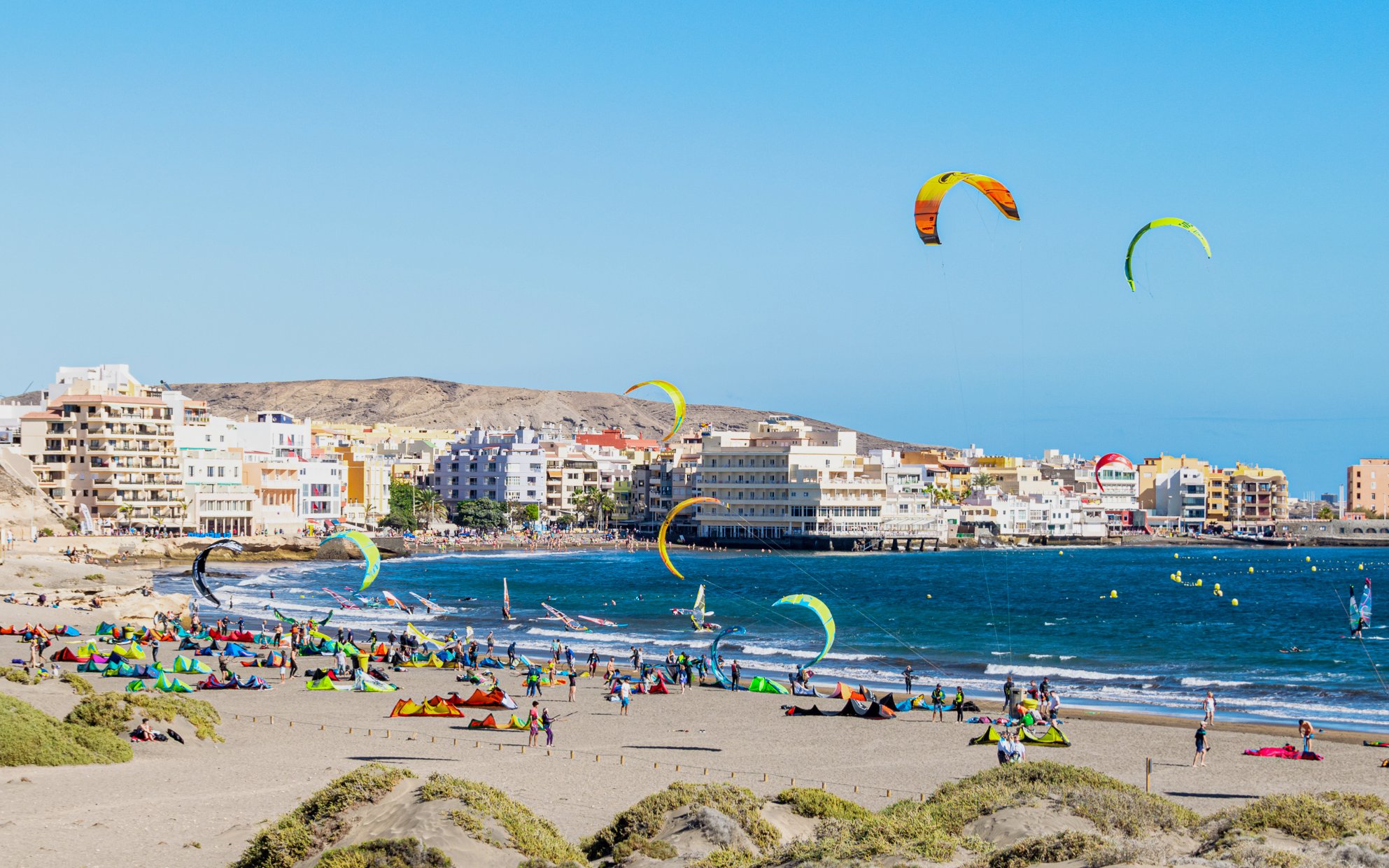 Kitesurfers at El Médano beach, Southern Coast of Tenerife, with colorful kites and coastal buildings.