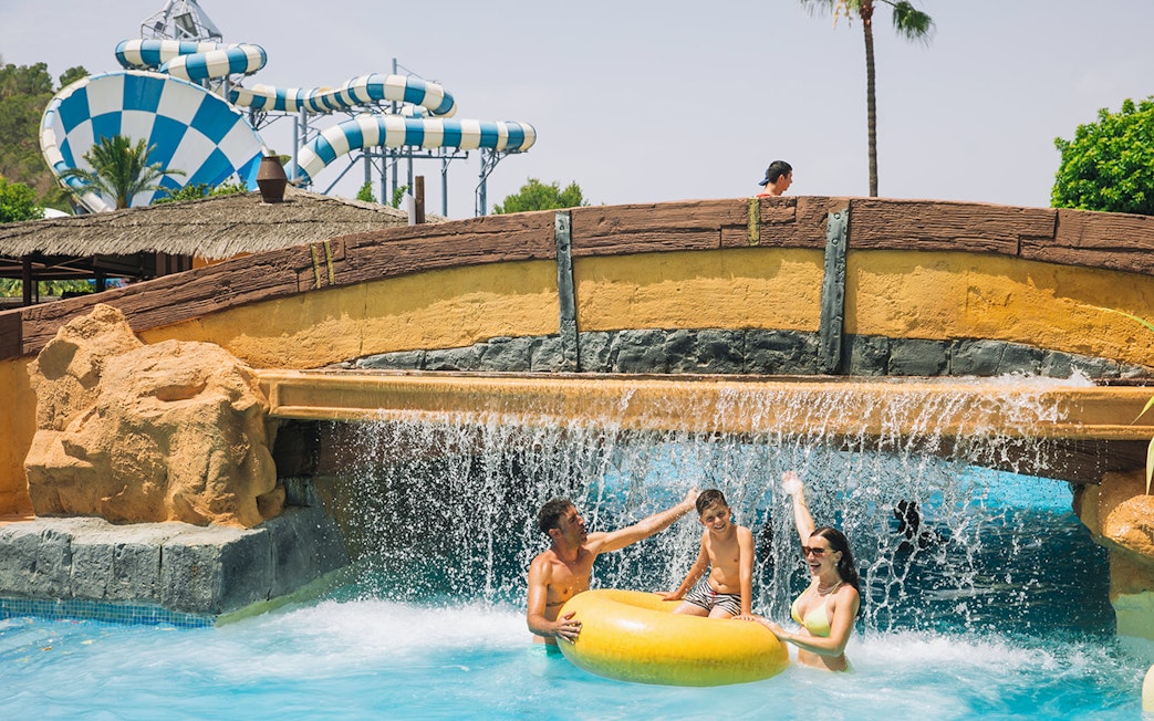 Family enjoying water ride under waterfall at Aqualandia Benidorm with slides in background.