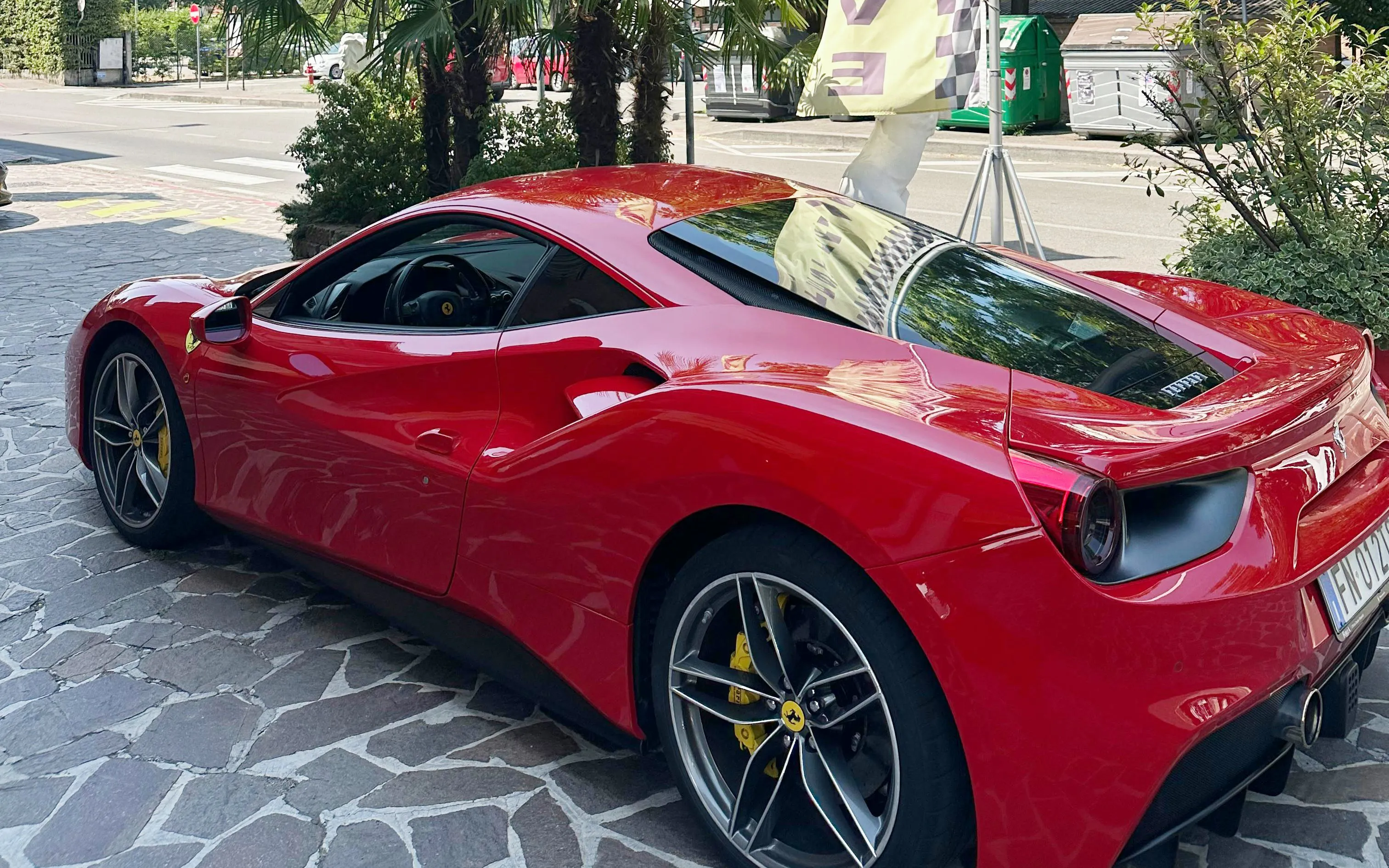 Red Ferrari 488 parked on a stone driveway in an urban setting.