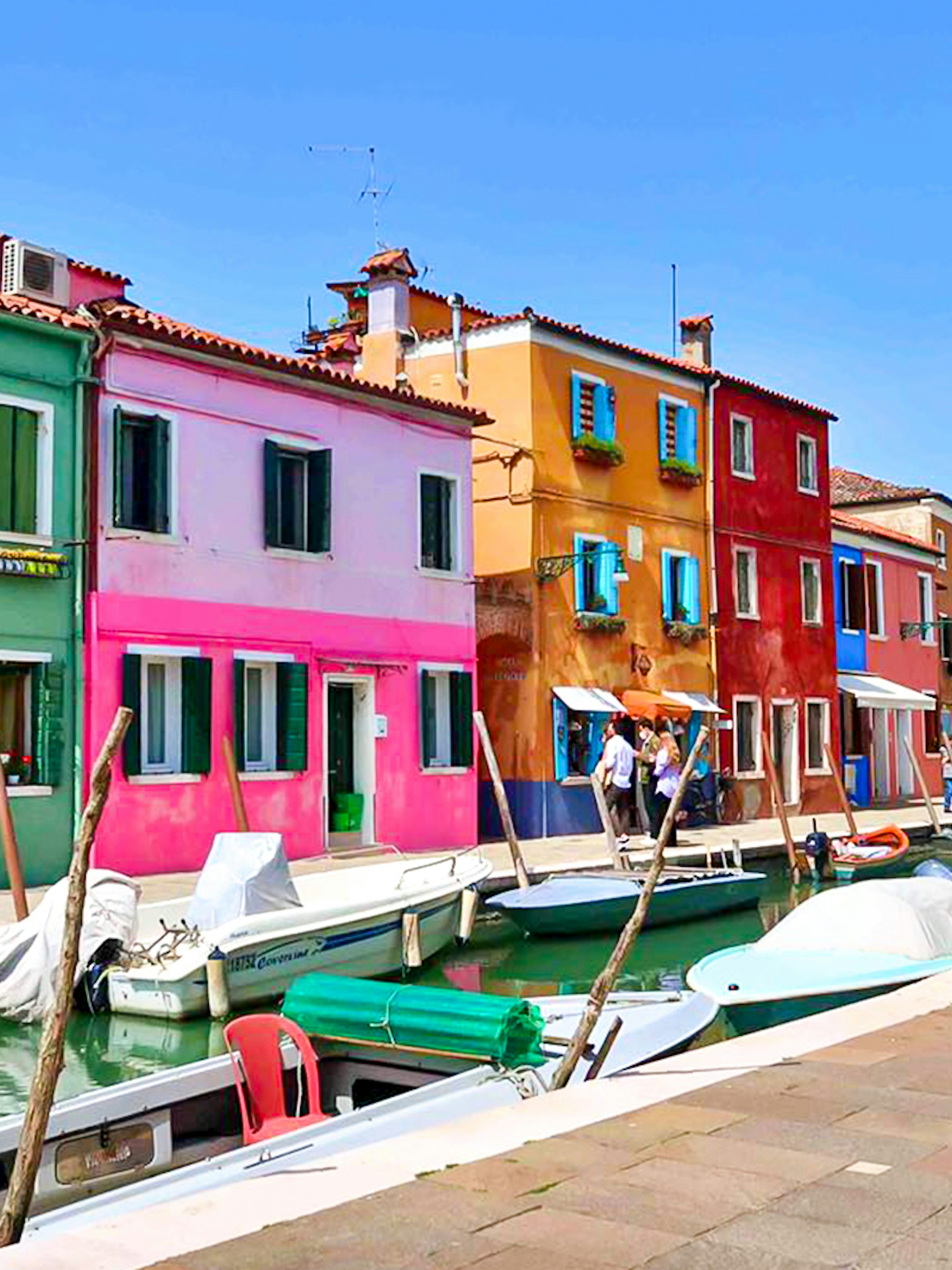 Colorful buildings along a canal in Burano, Italy, with boats docked nearby.