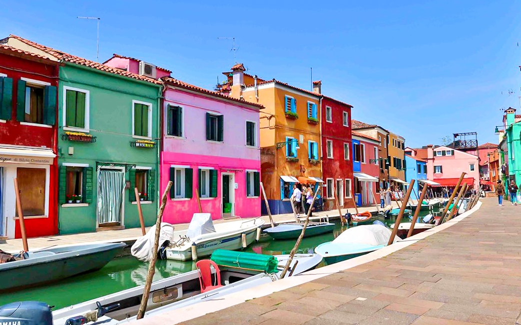Colorful buildings along a canal in Burano, Italy, with boats docked nearby.