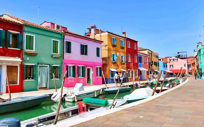 Colorful buildings along a canal in Burano, Italy, with boats docked nearby.