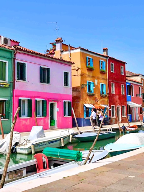 Colorful buildings along a canal in Burano, Italy, with boats docked nearby.