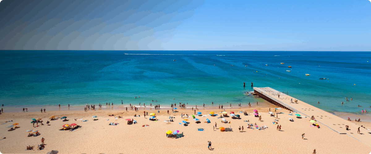 Beachgoers on Albufeira beach with colorful umbrellas and a pier extending into the ocean.